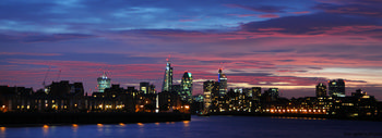 London centre sunset This urban landscape photograph shows the city centre of London during an autumn evening sunset, with the River Thames in the foreground reflecting city lights. The image captures prominent London architecture, including the Gherkin at 30 St Mary Axe and the Cheese Grater at 122 Leadenhall Street, both standing out among the illuminated buildings of the United Kingdom’s capital. The city skyline is silhouetted against vibrant sunset colours, emphasizing the architectural features and the urban character of central London along the River Thames.